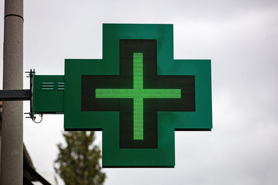 A green cross sign outside of a community pharmacy