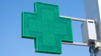 A green cross sign outside of a community pharmacy
