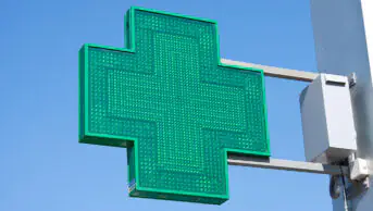 A green cross sign outside of a community pharmacy