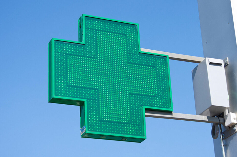 A green cross sign outside of a community pharmacy