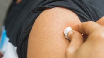 Physician cleans upper arm of patient ahead of vaccination