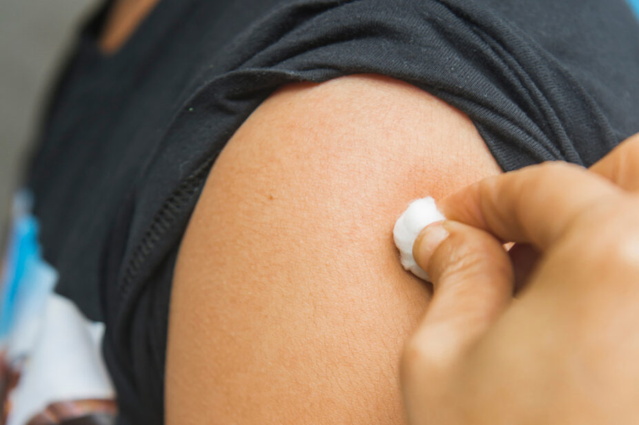 Physician cleans upper arm of patient ahead of vaccination