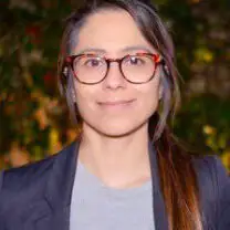 Baguiasri smiles wearing glasses and a suit in front of a green tree background