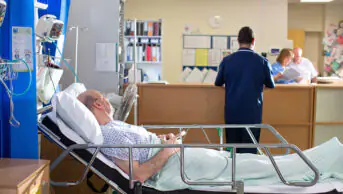 A hospital ward scene with a man in a bed, with clinicians in the background