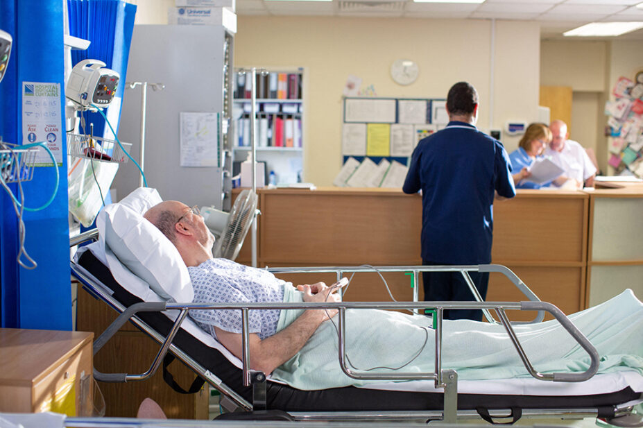 A hospital ward scene with a man in a bed, with clinicians in the background