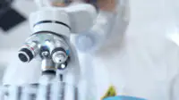 Professional scientist in protective gear is using microscope in a laboratory setting
