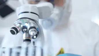 Professional scientist in protective gear is using microscope in a laboratory setting