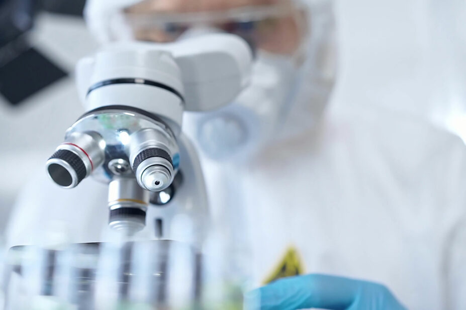Professional scientist in protective gear is using microscope in a laboratory setting