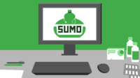 Green wall, grey desk, computer with SUMO logo on screen. On desk is keyboard, mouse, pens, pill packets and bottles