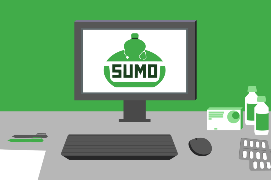Green wall, grey desk, computer with SUMO logo on screen. On desk is keyboard, mouse, pens, pill packets and bottles