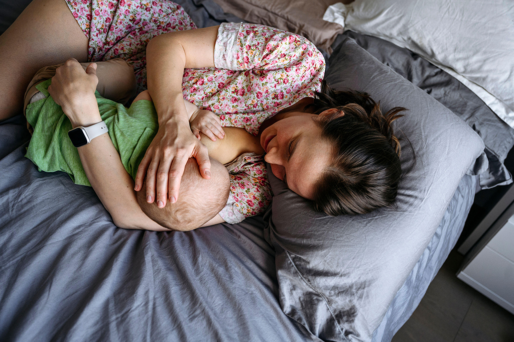 Breastfeeding woman and baby lie on a blue/grey bed