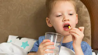 A child takes a tablet with a glass of water