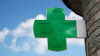 A green cross sign outside of a community pharmacy