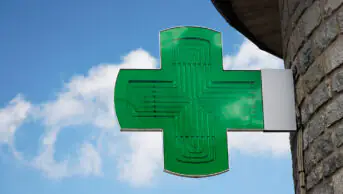 A green cross sign outside of a community pharmacy