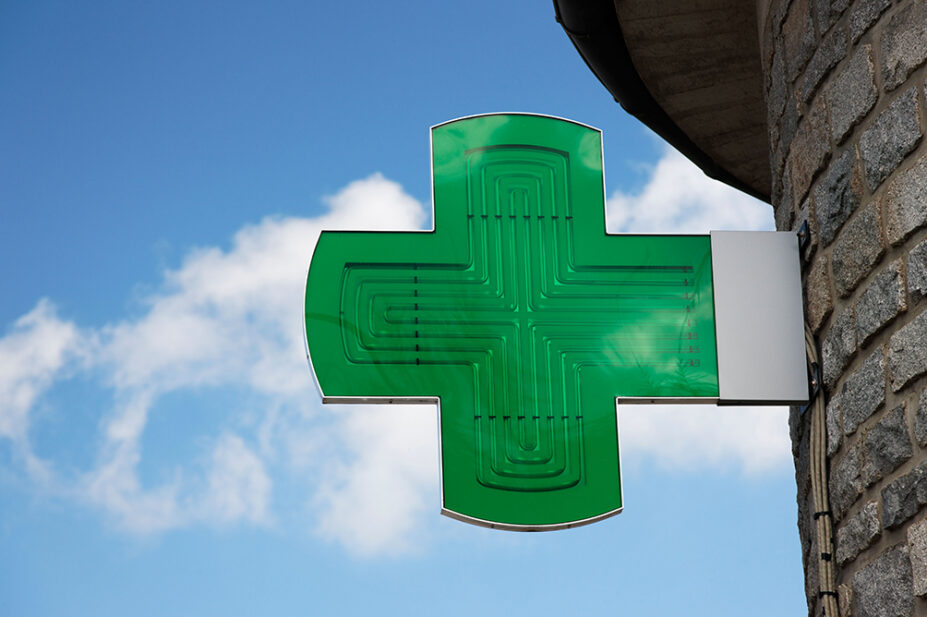 A green cross sign outside of a community pharmacy