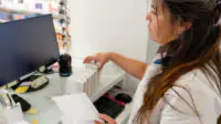 A pharmacist arranges medications at the front desk of a pharmacy