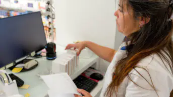 A pharmacist arranges medications at the front desk of a pharmacy