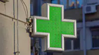 A green cross sign outside of a community pharmacy