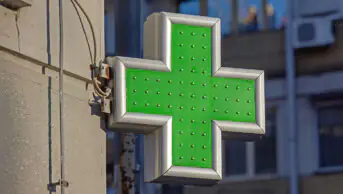 A green cross sign outside of a community pharmacy