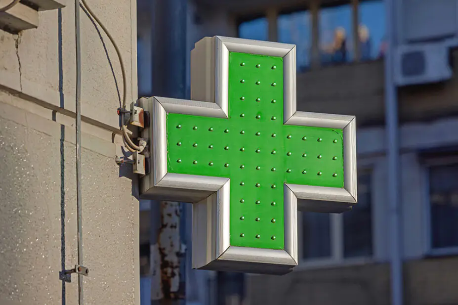A green cross sign outside of a community pharmacy