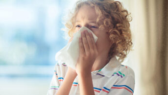 A child with allergies blows his nose with a tissue