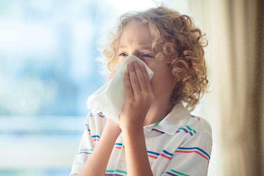 A child with allergies blows his nose with a tissue