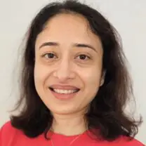 Namita smiles in front of a plain white background, wearing a coral coloured top