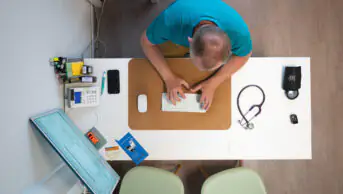 Birds-eye view of a male GP working at a desk, typing on a keyboard.