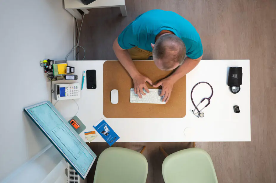 Birds-eye view of a male GP working at a desk, typing on a keyboard.