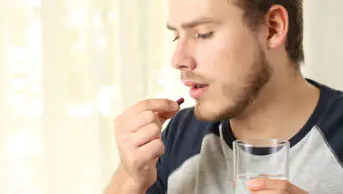 A man takes a tablet with a glass of water