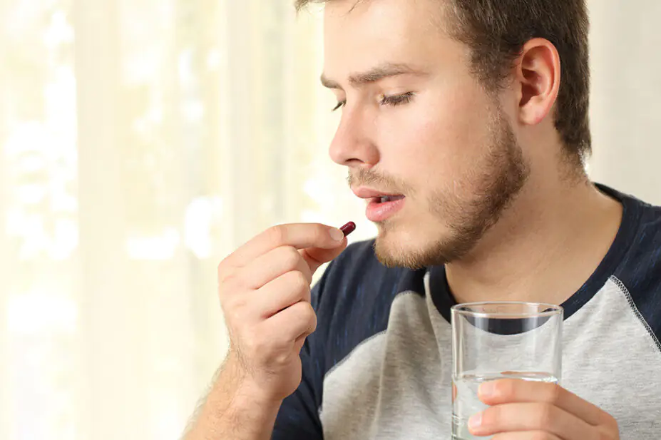 A man takes a tablet with a glass of water