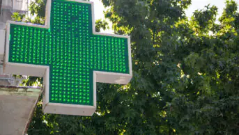 A green cross sign outside of a community pharmacy