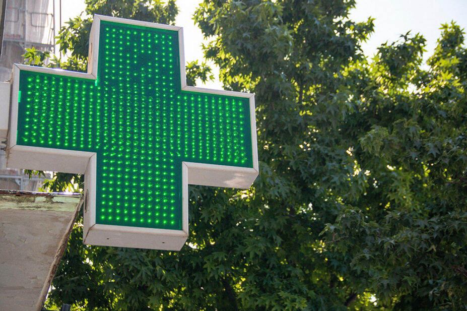 A green cross sign outside of a community pharmacy
