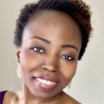 Gospel smiles wearing gold earrings in front of a grey / neutral background