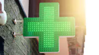 A green cross sign outside of a community pharmacy