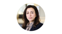 Round image of Amira looking serious in a shirt and blazer on a white background