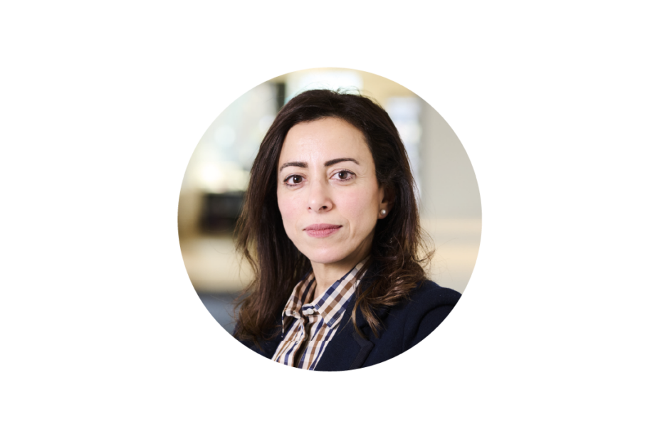 Round image of Amira looking serious in a shirt and blazer on a white background
