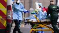 Medics wearing PPE transport a patient into the emergency department of the Royal London Hospital in London, England