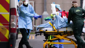 Medics wearing PPE transport a patient into the emergency department of the Royal London Hospital in London, England