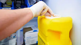 A healthcare professional disposes of waste in a sharps bin