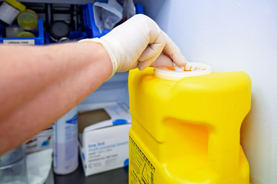 A healthcare professional disposes of waste in a sharps bin
