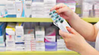 A pharmacist looks at a blister pack of medicine in the aisle of a community pharmacy