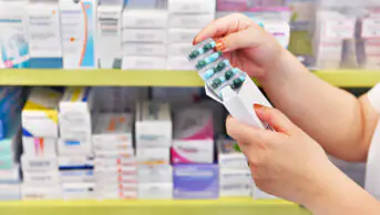 A pharmacist looks at a blister pack of medicine in the aisle of a community pharmacy