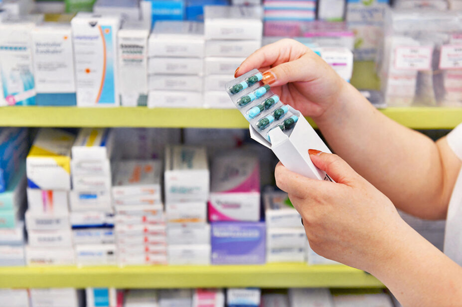 A pharmacist looks at a blister pack of medicine in the aisle of a community pharmacy