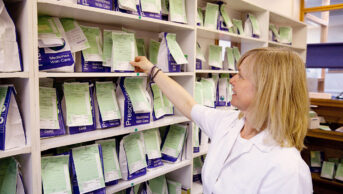 A pharmacist reaches for a prescription in a community pharmacy