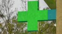 A green cross sign outside of a community pharmacy