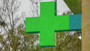 A green cross sign outside of a community pharmacy