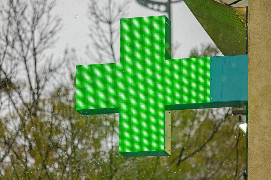 A green cross sign outside of a community pharmacy