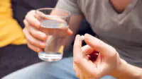 A man takes a tablet with a glass of water