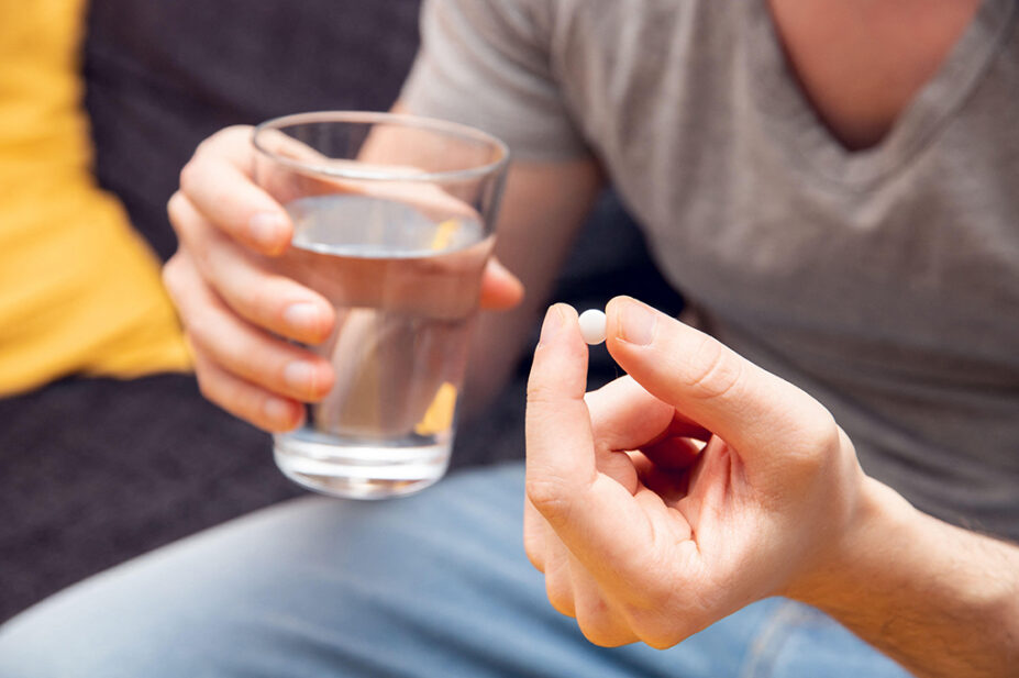 A man takes a tablet with a glass of water